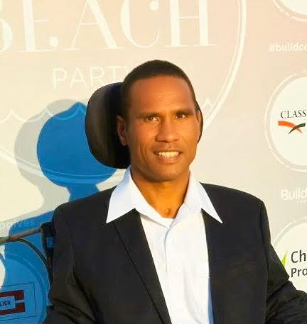Profile photo of Mark, wearing a black suit and white shirt, in front of a background that says "Beach Party"
